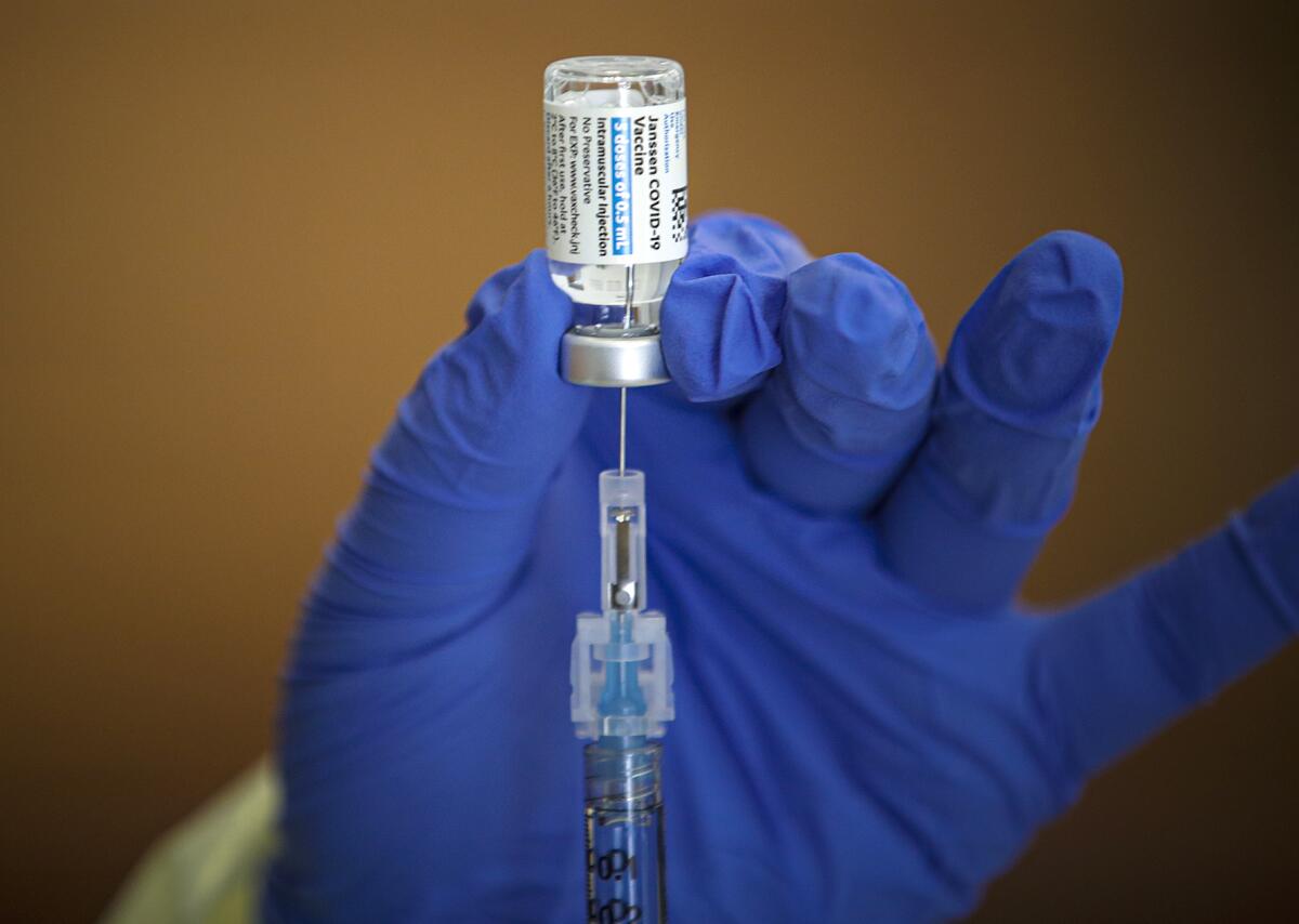 Gloved hands pull a COVID-19 vaccine dose out of the vial and into a syringe