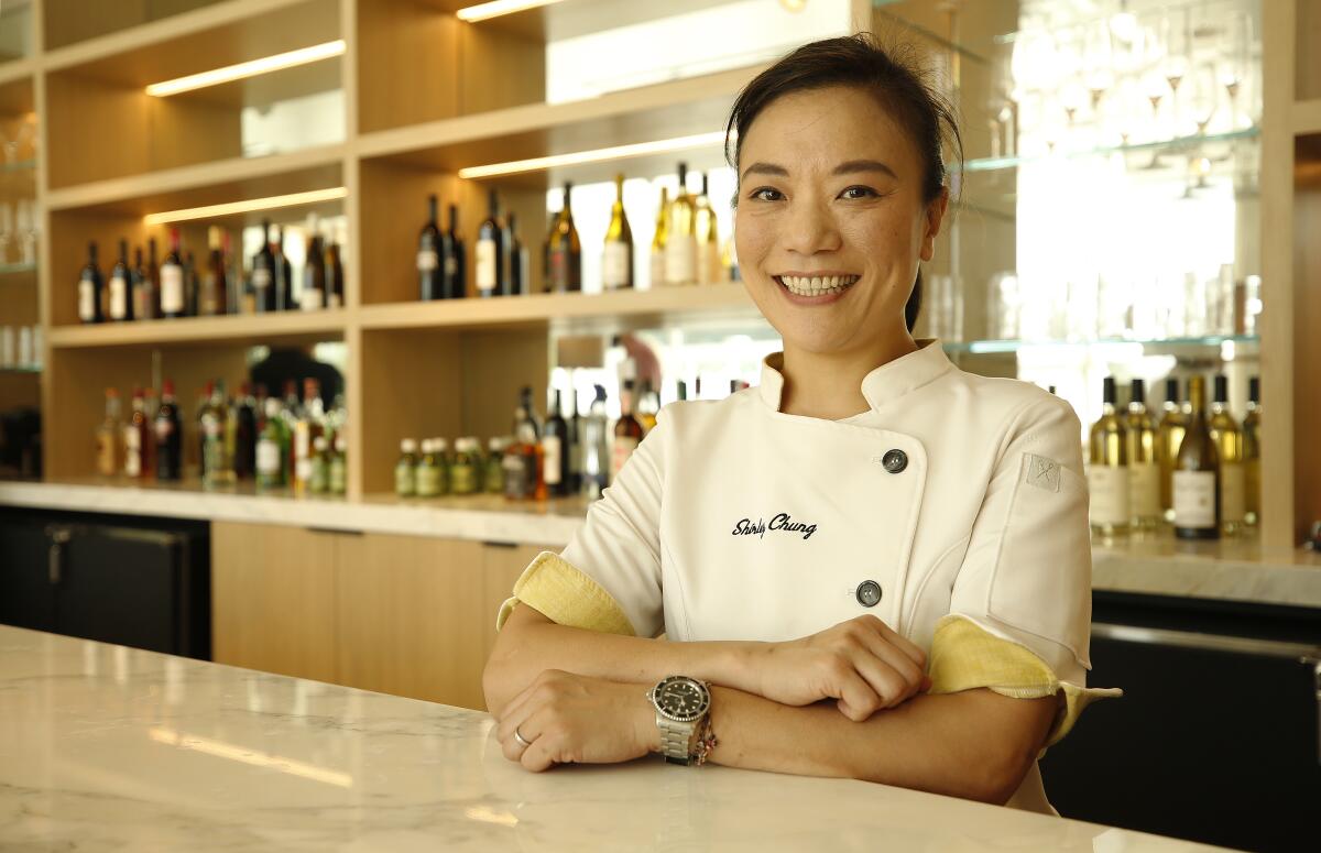 Shirley Chung smiling in chef's whites with her arms crossed in front of her on a light stone countertop