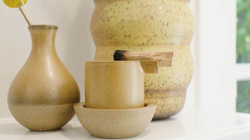 A beige ceramic vase on a table next to a beige ceramic cup-like ashtray