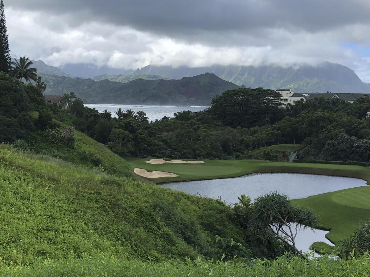 A dark sky above mountains and a golf course covered in deep green grass and trees.