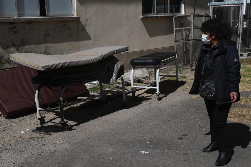 Herminia Carpio looks at the body of her brother Guillermo covered by a slim mattress outside the General Hospital before his body is taken away by a funeral home in La Paz, Bolivia, Wednesday, July 22, 2020. Carpio said her 58-year-old brother died the previous afternoon, and according to the hospital he died of COVID-19. (AP Photo/Juan Karita)