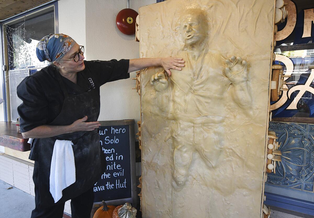 A woman stands and places one hand on a life-sized bread sculpture of Han Solo