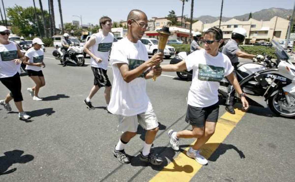 Torch bearer Ronie Moreno get some help with the torch from Parking Enforcement officer Maria Castro at the start of the Glendale leg of the Special Olympics Torch Run.