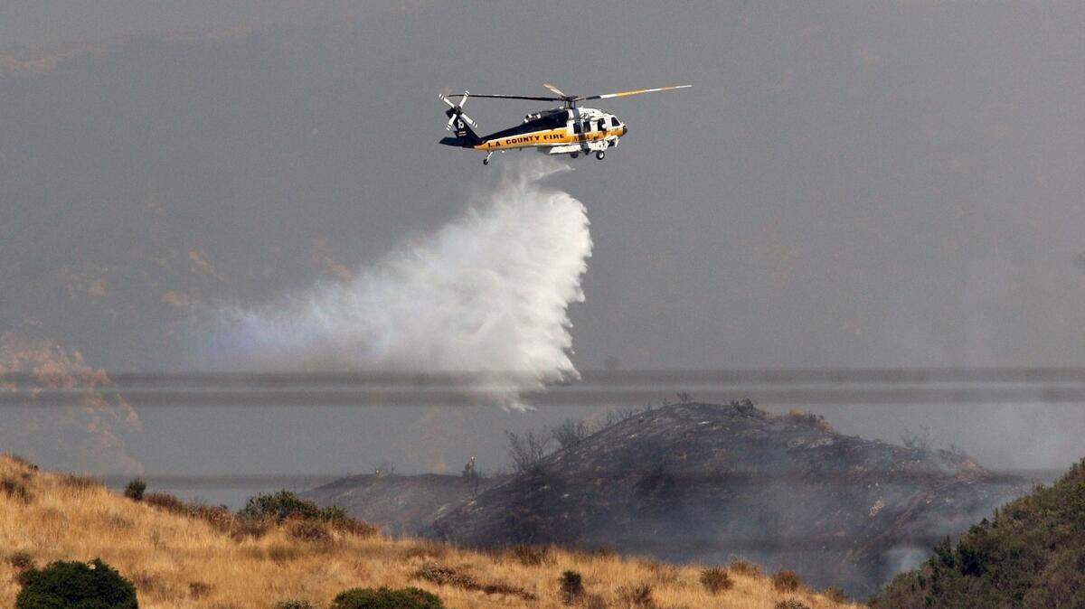 A helicopter drops water to fight a brush fire that broke out near the Burbank Police Department's shooting range on Wednesday, July 26, 2017.