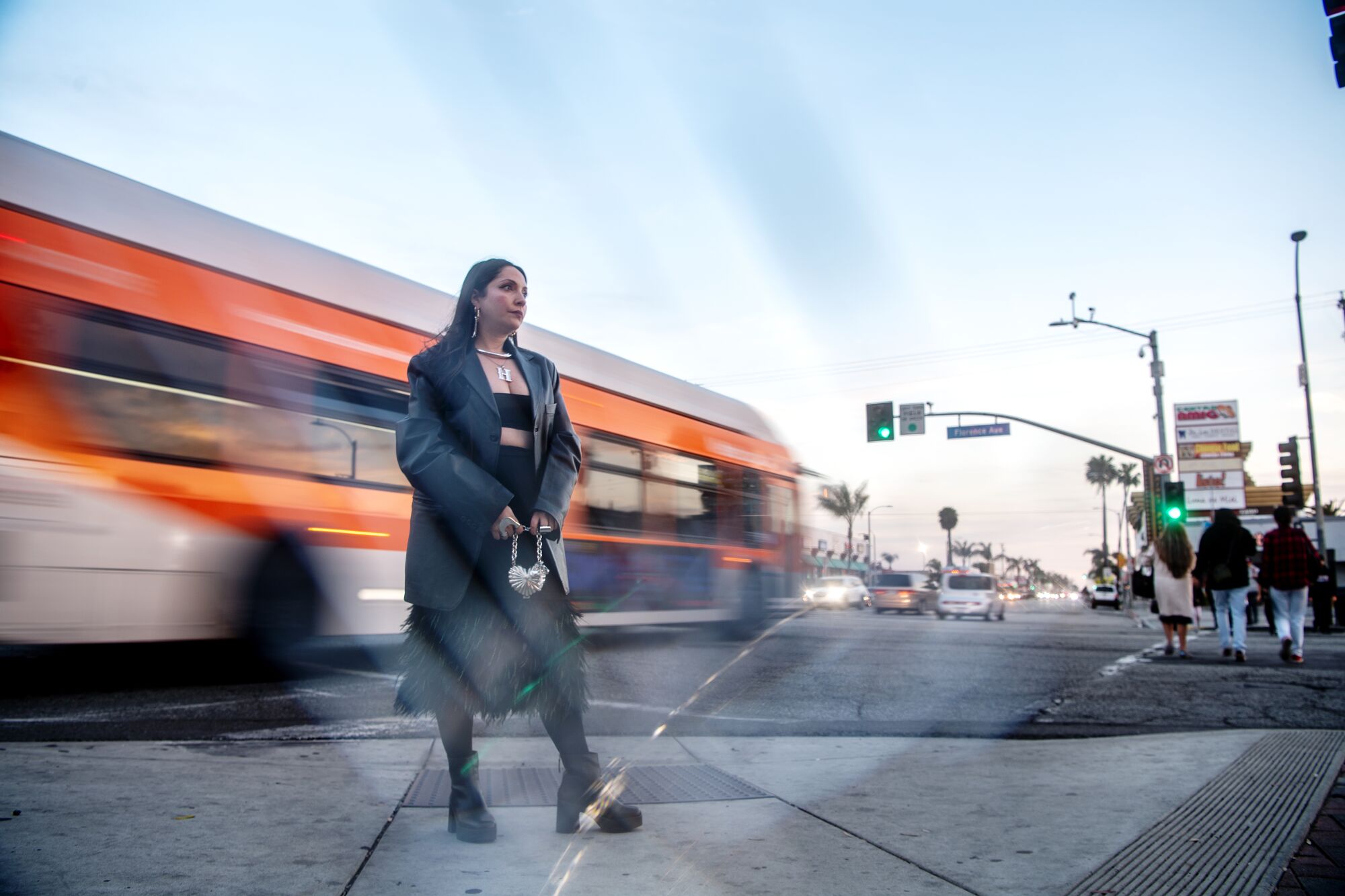 A bus blurs past as a woman stands on a sidewalk.