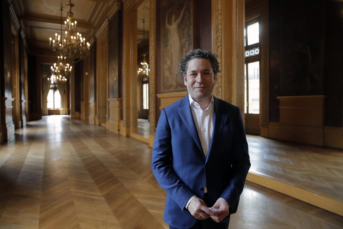 Gustavo Dudamel stands in an elegant wood-lined room with chandeliers inside the Palais Garnier 