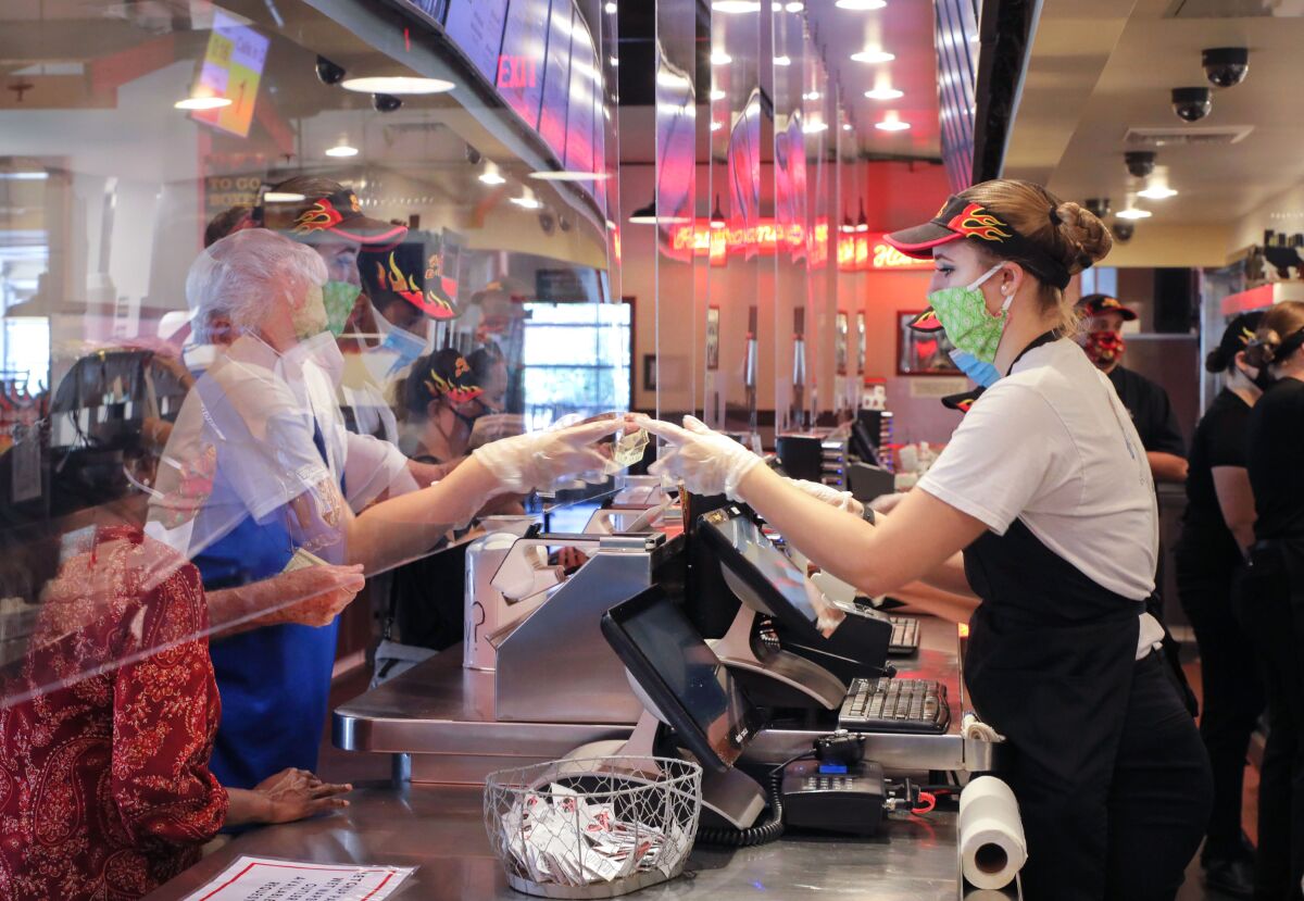 A masked employee at Phil's BBQ Rancho Bernardo location serves take-out customers behind clear plastic panels. 
