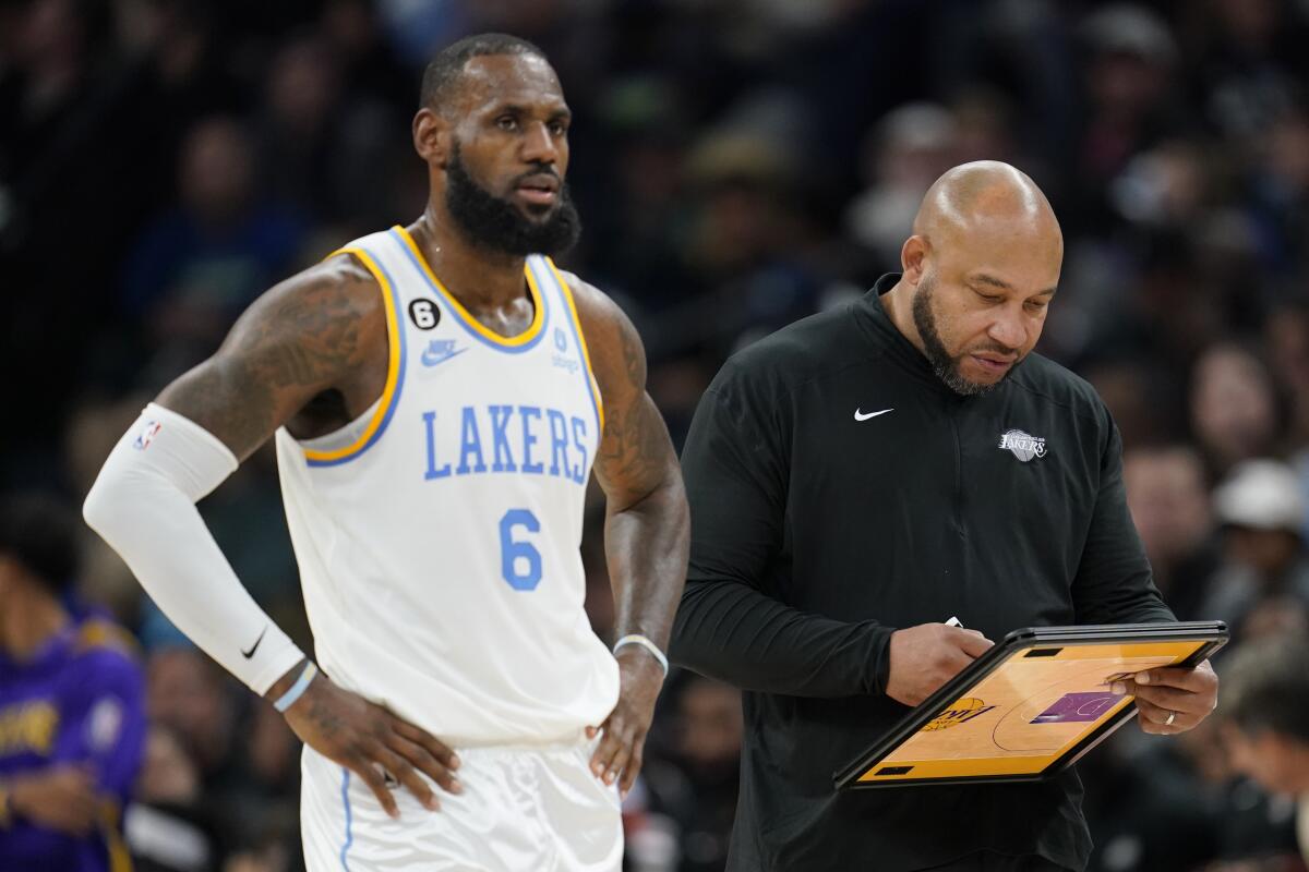 Lakers forward LeBron James stands on the court as coach Darvin Ham looks at a play on his clipboard.