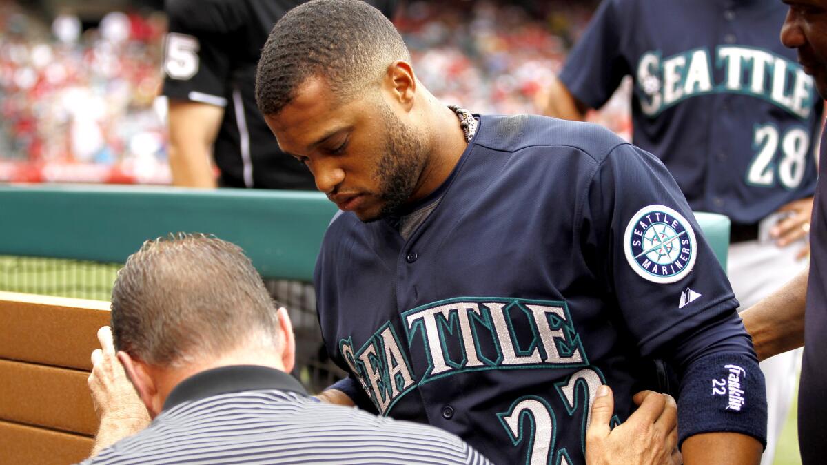 Mariners second baseman Robinson Cano (22) is led from the dugout by trainer Rob Nodine after getting hit in the forehead with an errant throw by an Angels player during warmups in the seventh inning Saturday.