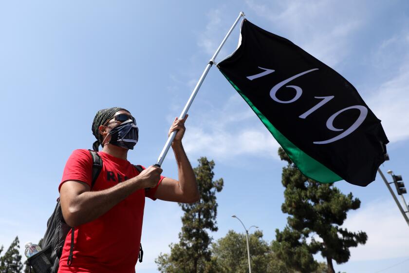 LOS ANGELES, CA - JUNE 19: Mark Austin, of Van Nuys, carries a flag with the year 1619, the year the first African slave was brought to the United States, while marching in the Juneteenth "Black Lives Liberating the Black Community" Caravan/March along Martin Luther King Blvd ending at the Baldwin Hills Crenshaw Plaza on Friday, June 19, 2020 in Los Angeles, CA. (Gary Coronado / Los Angeles Times)