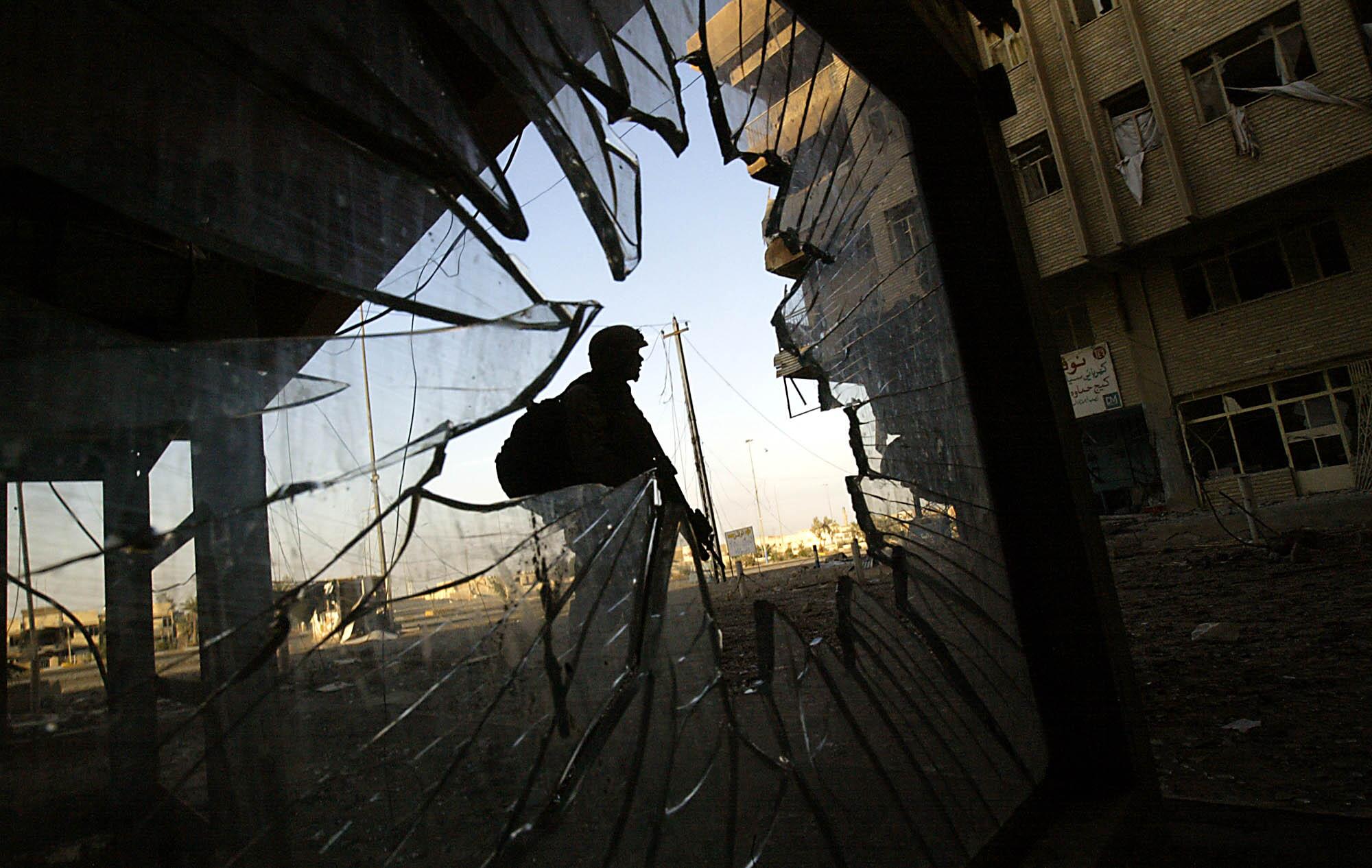 A Marine stands guard, seen through a hole in shattered glass