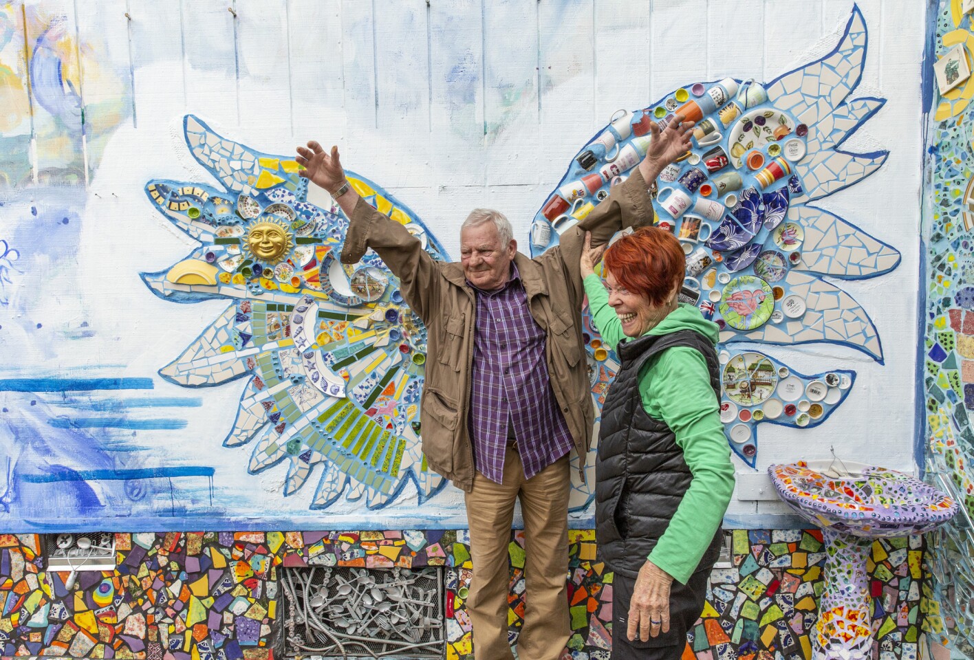 Artist Cheri Pann helps guest Bernard Giraux pose with mosaic tile wings at the Mosaic Tile House, which she and her husband own.