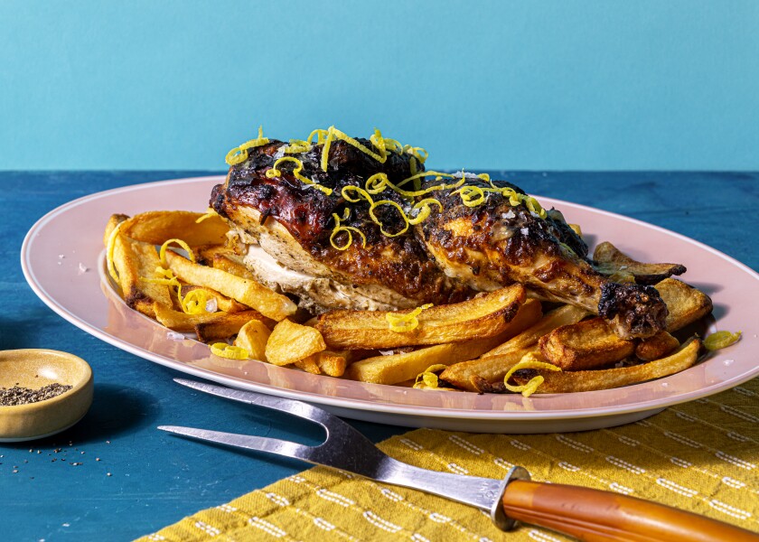 A grilled half-chicken decorated with lemon zest sits atop a bed of french fries.