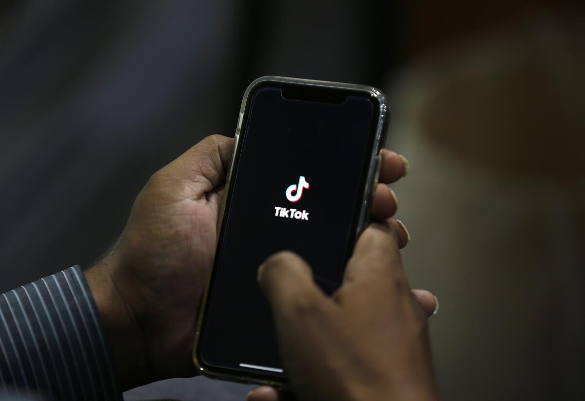 A pair of hands holds a cellphone with the TikTok logo on the screen.