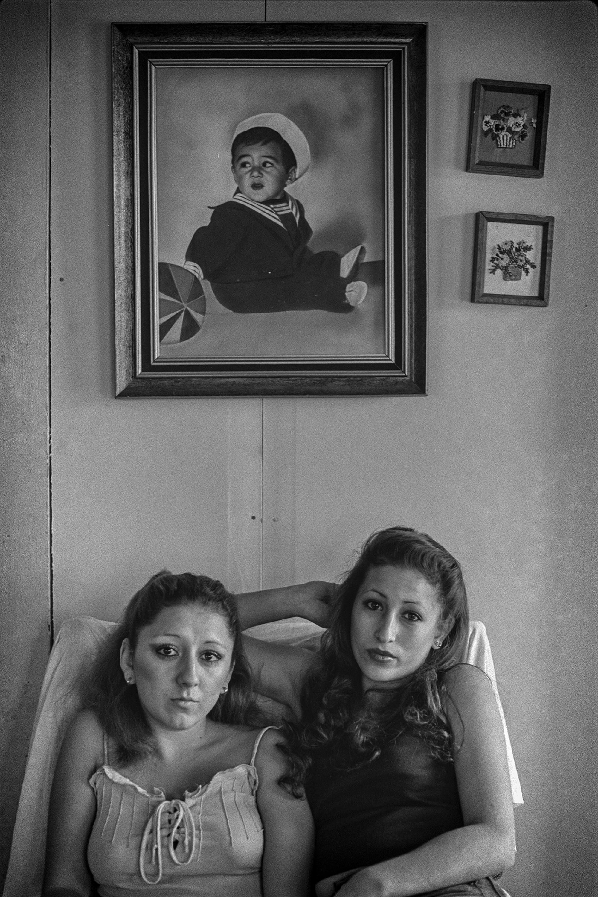 A photo of two women sitting under a portrait of a baby boy.