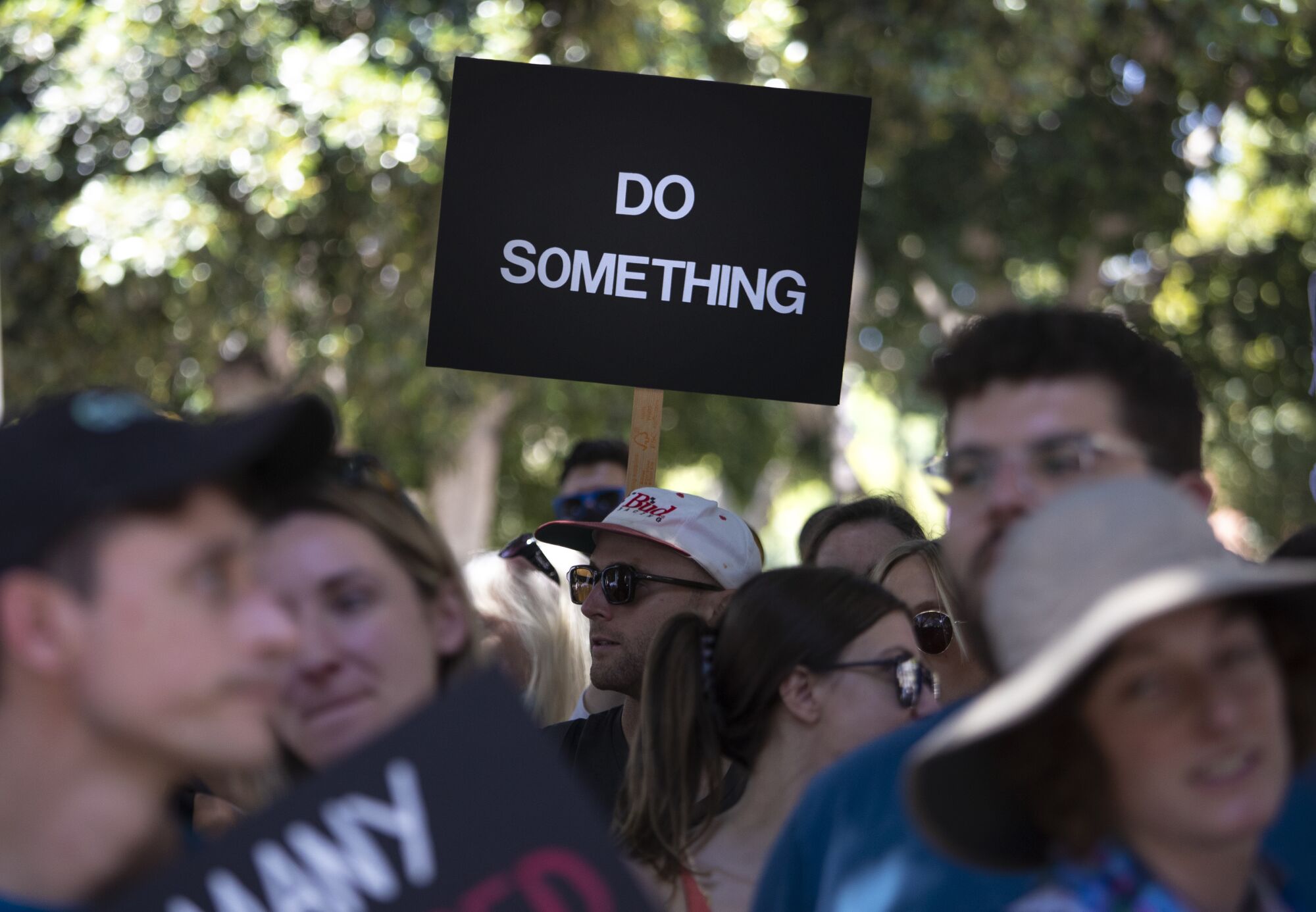 People stand together. One holds a sign reading "Do something."