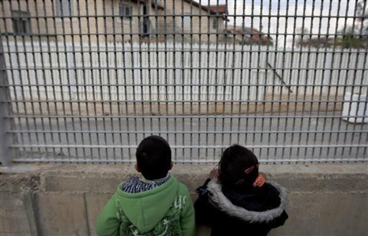 In this photo taken Wednesday, Feb. 9, 2011 Palestinian boys look through the bars of the fenced-in house of al-Ghirayim family between the Jewish settlement of Givon Hahadasha and the West Bank village of Beit Ijza. The al-Ghirayib family lives in one of the stranger manifestations of Israel's 43-year occupation of the West Bank: a Palestinian house inside a metal cage inside an Israeli settlement. The family's 10 members, four of them children, can only reach the house via a 40-yard (meter) passageway connecting them to the Arab village of Beit Ijza below. The passage passes over a road frequented by Israeli army jeeps and is lined on both sides with a 20-foot-high (6-meter) heavy-duty metal fence.(AP Photo/Sebastian Scheiner)