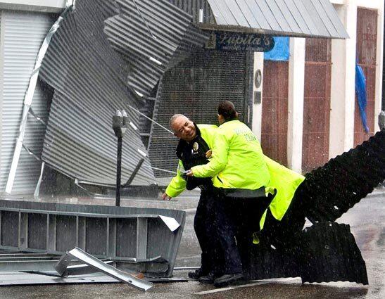 Brownsville, Texas, police officers duck debris blown by Hurricane Dolly as they try to move an awning out of a downtown street.