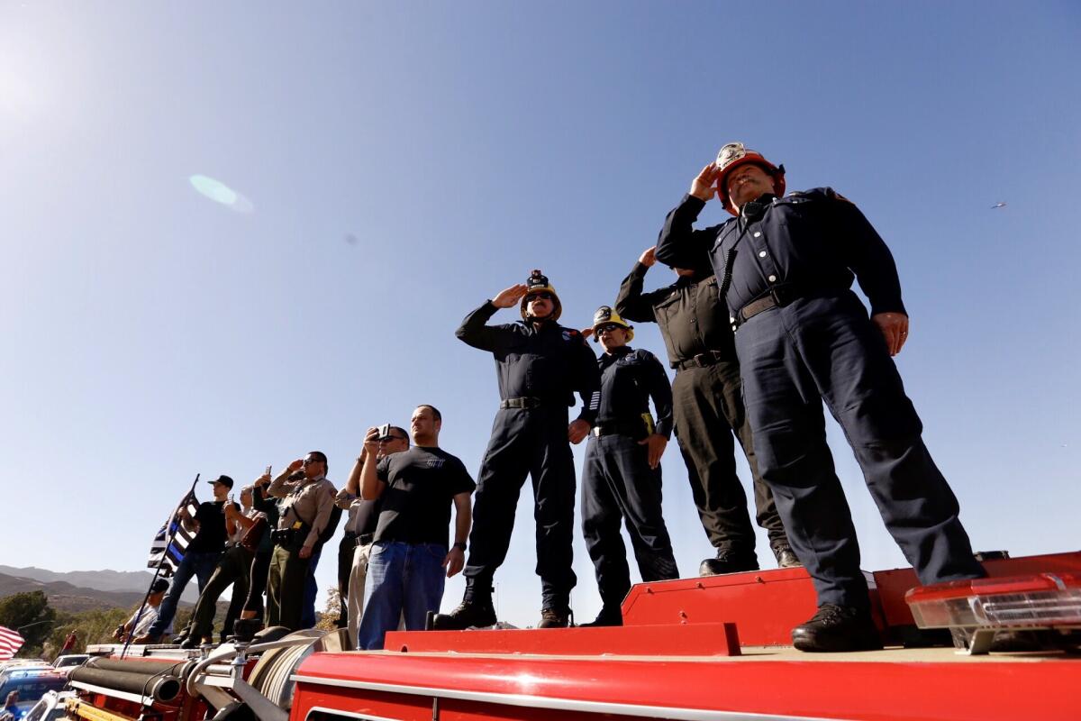 Firefighters give a salute as the hearse carrying the casket of Ventura County sheriff's Sgt. Ron Helus heads north on the 101 Freeway.