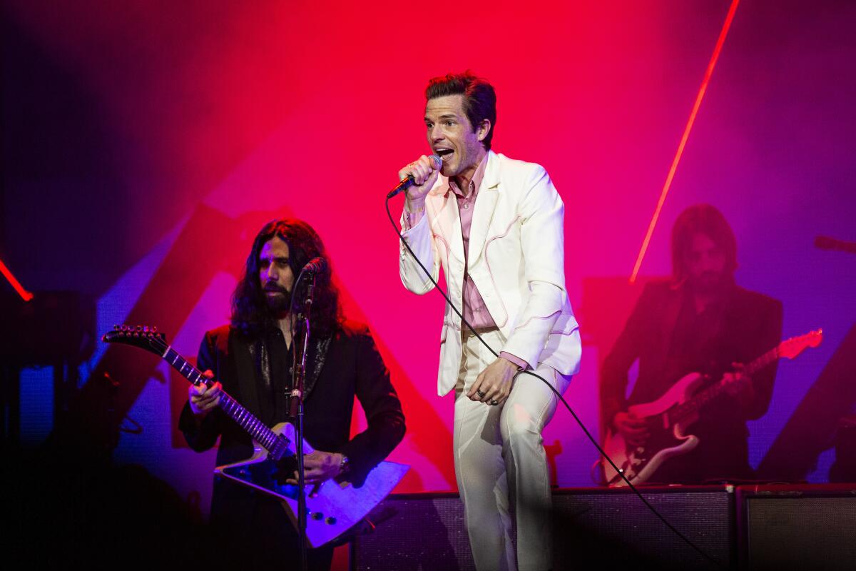 A man in a white suit performs alongside other members of the band who are wearing black pants and jackets 