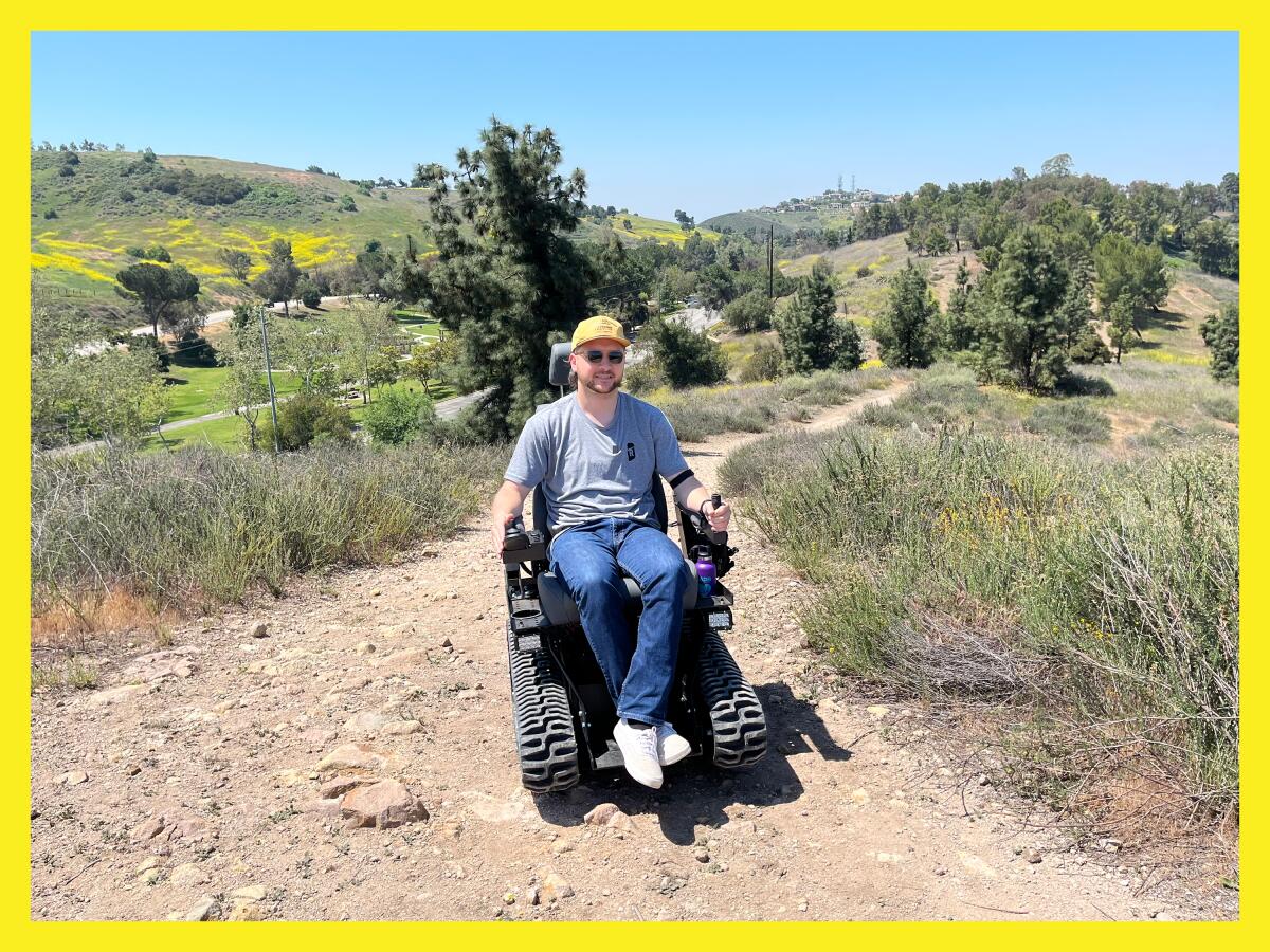 photo of a man on a hiking trail on a sunny day sitting in an electric wheelchair with thick treads.