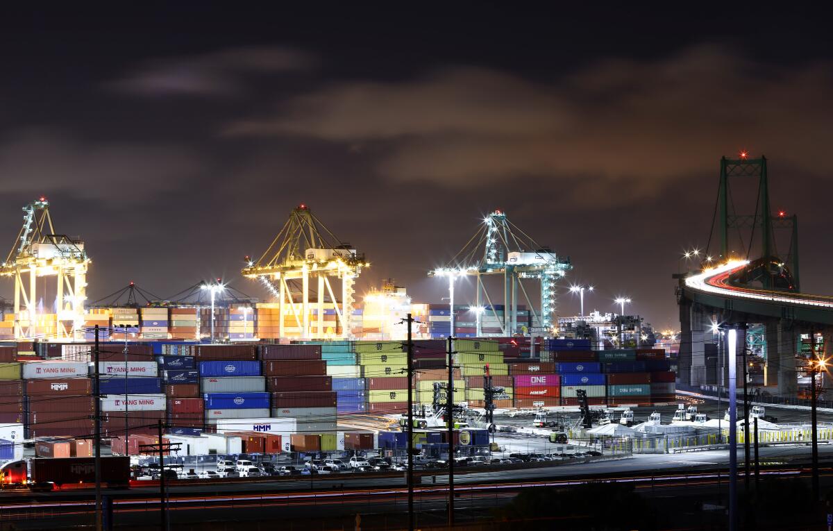 Shipping containers piled high at the Port of Los Angeles at nighttime.