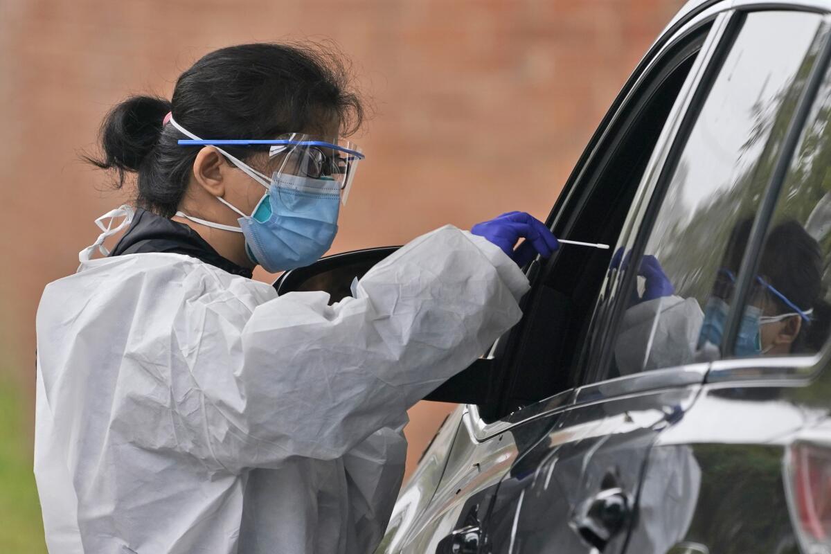 A woman in protective gear hands a test swab through a car window