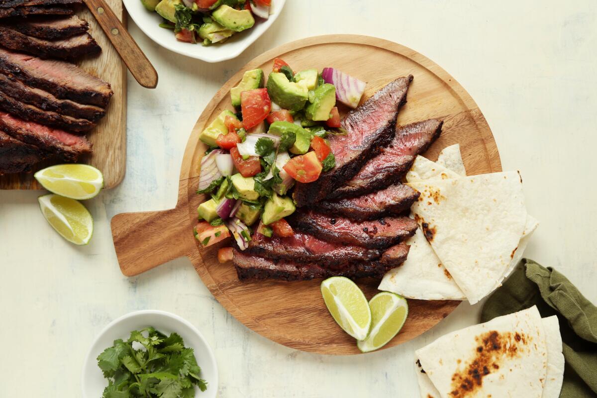 Grilled steak with guacamole salad is laid out on a wooden plate, garnished with slices of lemon and lime 