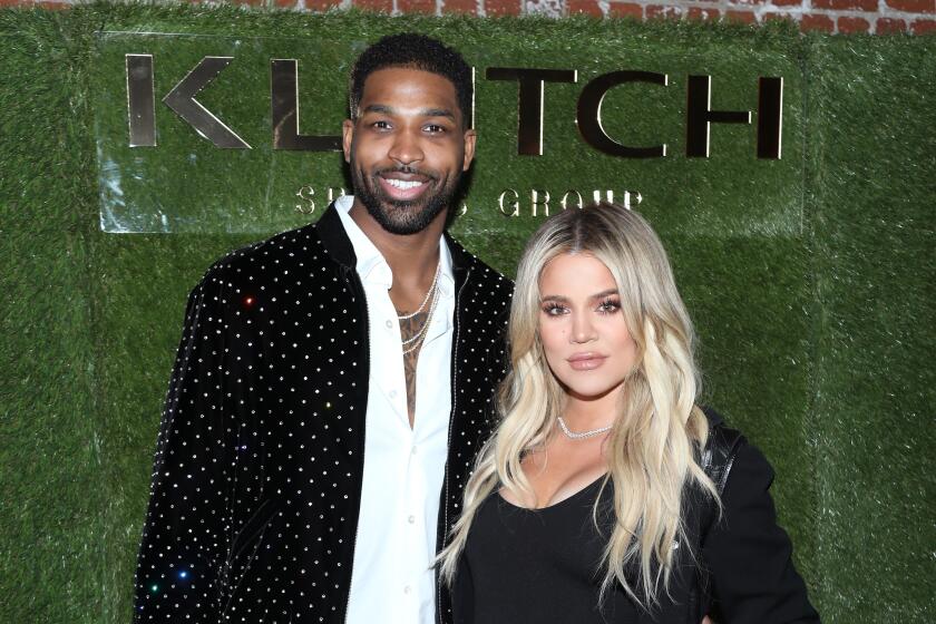 Tristan Thompson and Khloé Kardashian wearing dark clothing in front of a fake grass backdrop