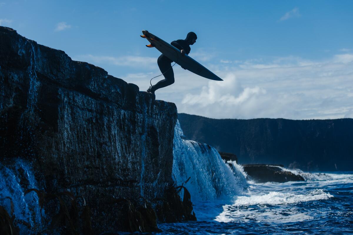 Un surfeur est accroupi sur une falaise au bord de l'océan.