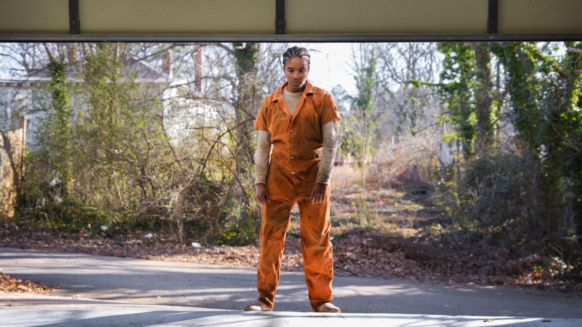 Tiffany Haddish stands, wearing orange overalls