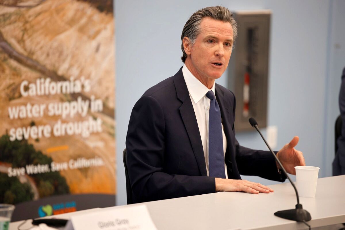 Gov. Gavin Newsom speaks in front of a sign that says, "California's water supply in severe drought"