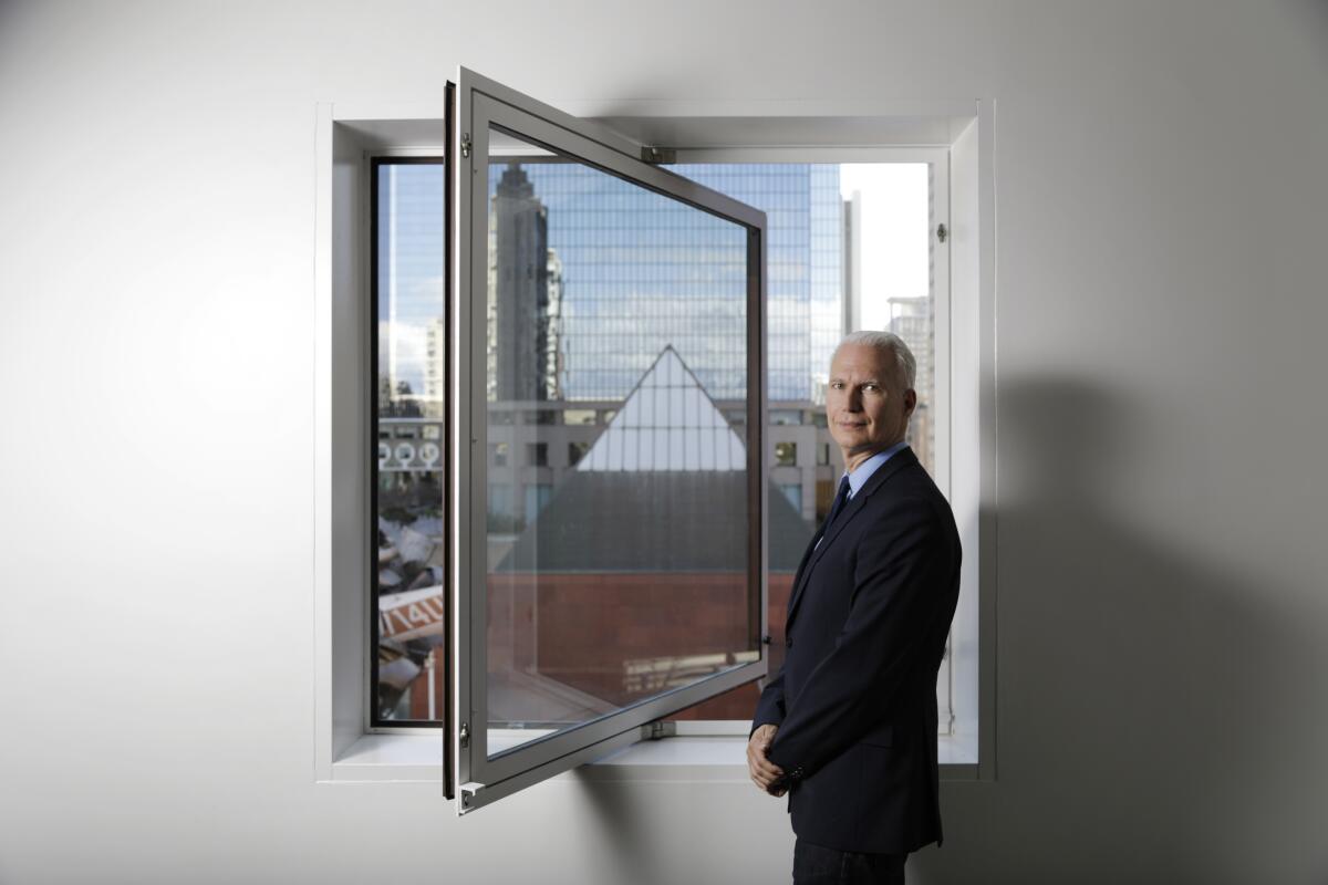 A man in a suit stands by an open window.