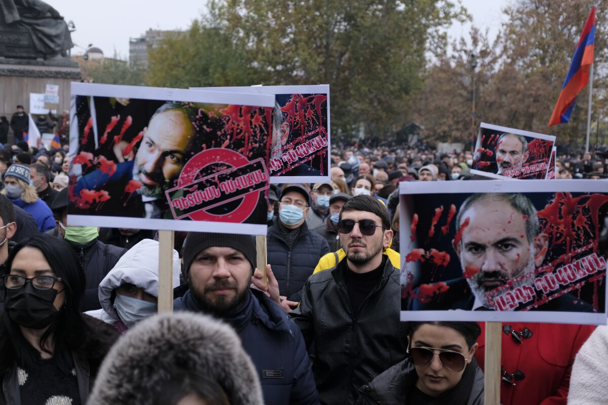 Demonstrators hold posters of Armenian Prime Minister Nikol Pashinyan with red painted hands and splashes over his face.