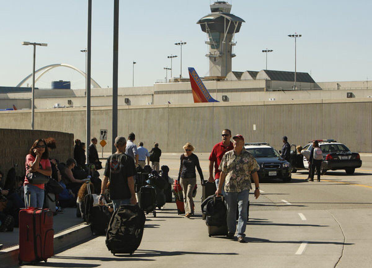 Passengers evacuated from LAX terminals walk with their luggage after a gunman opened fire inside Terminal 3.