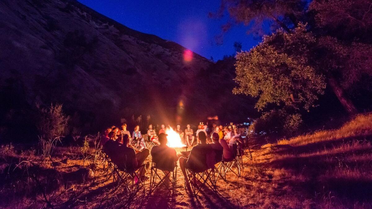 After a fun day of rafting on the Tuolumne River near Yosemite National Park, and a tasty dinner, a group of OARS rafters gather cozily around a fire pit.