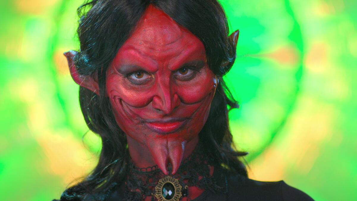 A woman in red devil makeup and prosthetics