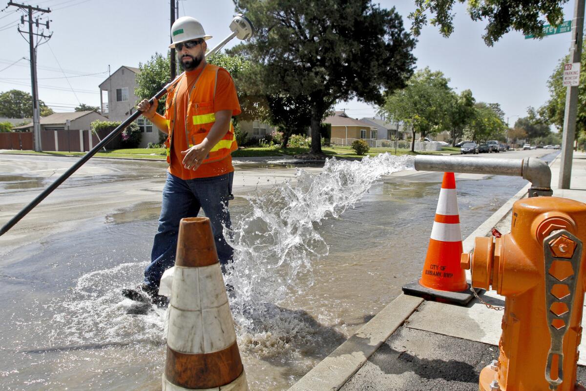 Burbank Water and Power land surveyor Carlos Sanchez walks past a hydrant releasing water pressure near a broken water main at the Burbank Fire Department training center on Wednesday, June 18, 2014.