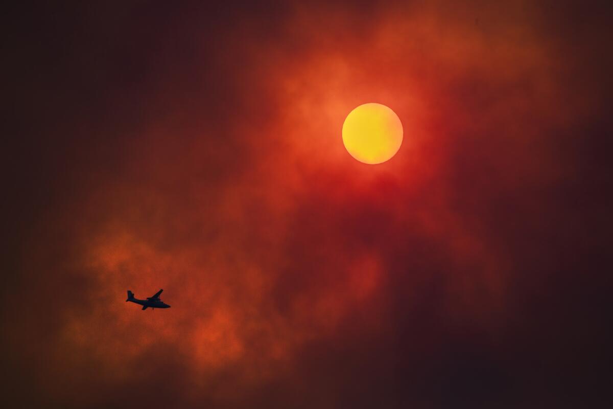 Heavy smoke obscures the sun as a firefighting aircraft works the Holy fire burning in Cleveland National Forest above Lake Elsinore.