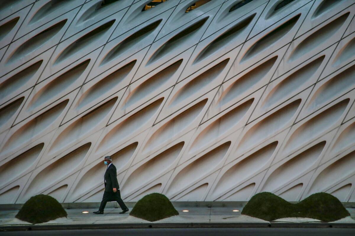 A man in a suit and a face mask walks in front of the Broad Museum.