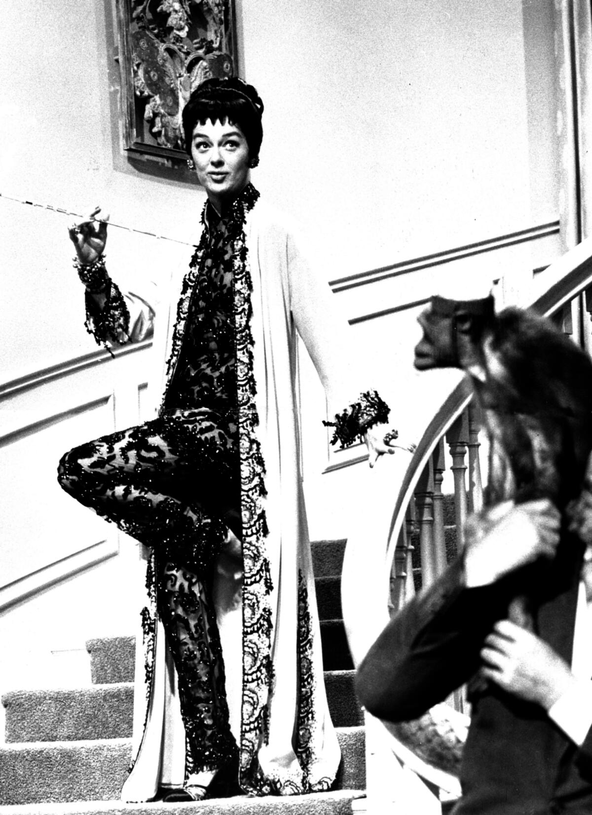 Rosalina Russell wearing a lace bodysuit and a silk robe descends a dramatic staircase in a scene from "Auntie Mame." 