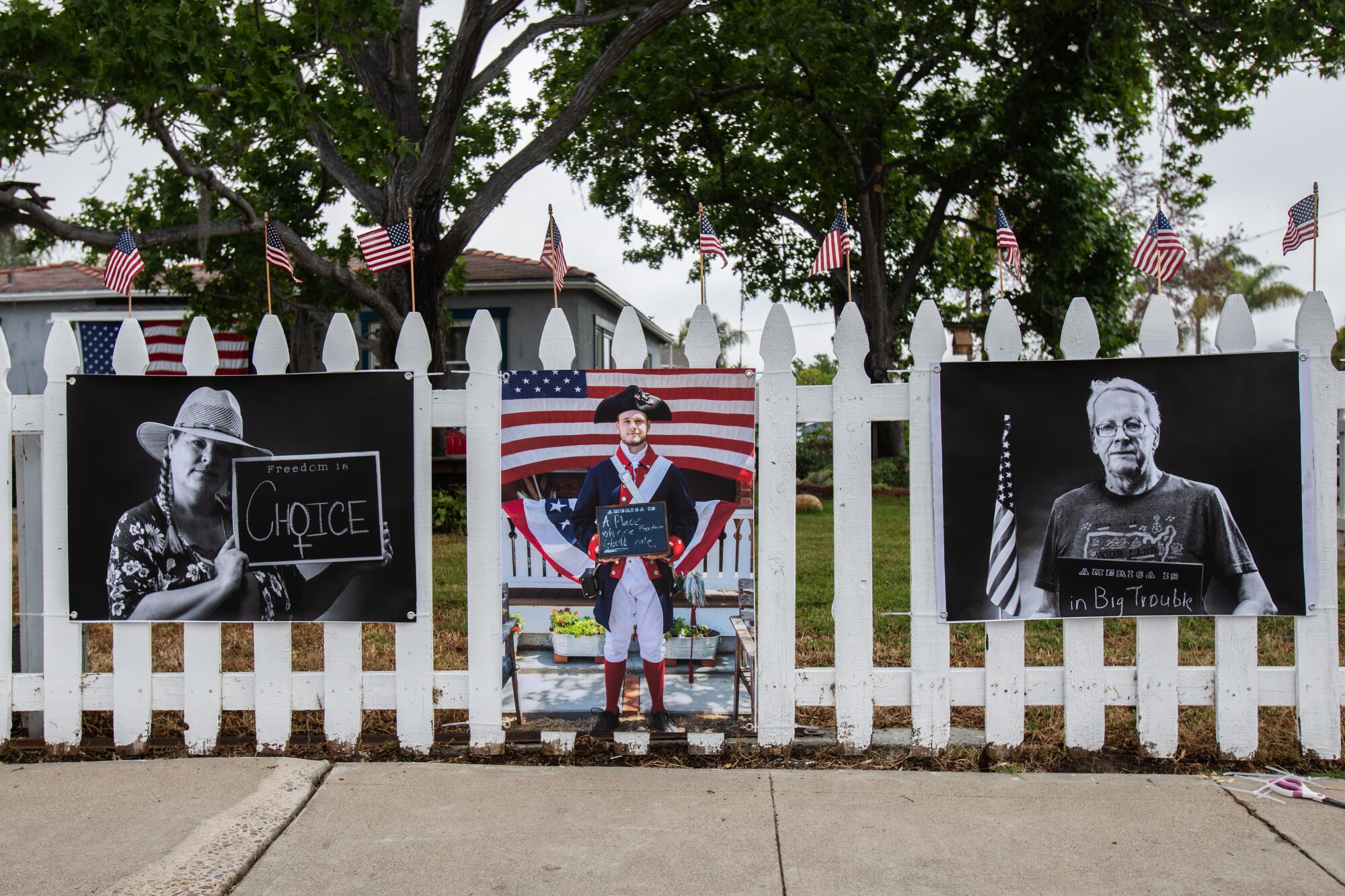 Todd Bradley hangs up portraits along a white picket fence with American flags on it