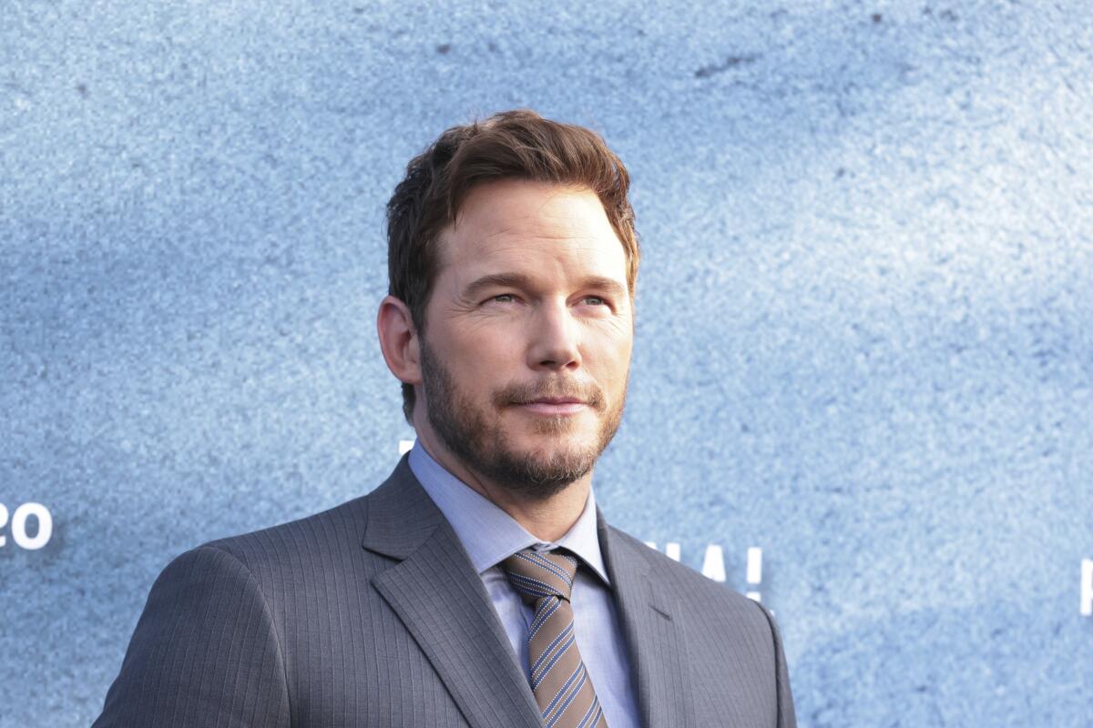 Chris Pratt in a grey suit and tie posing at a red carpet event