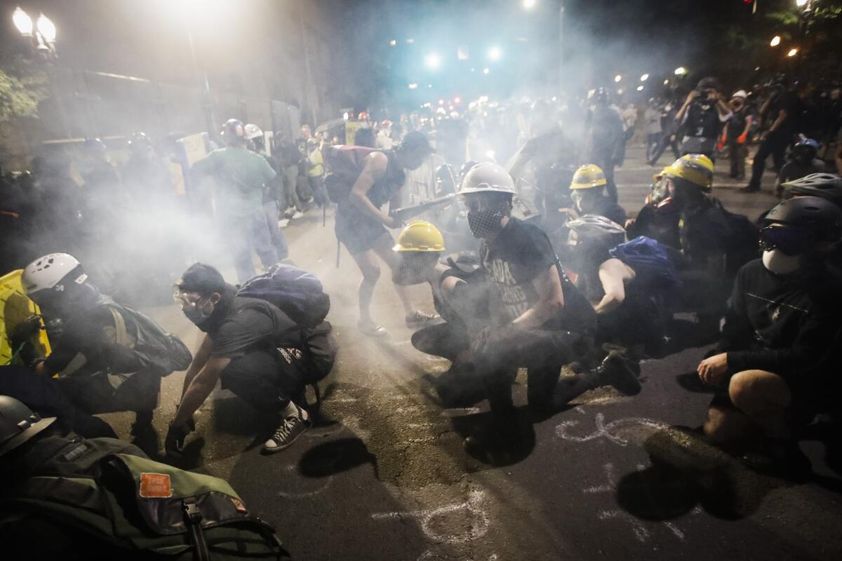 Los manifestantes se sientan y arrodillan mientras el gas lacrimógeno llena el aire durante una protesta.