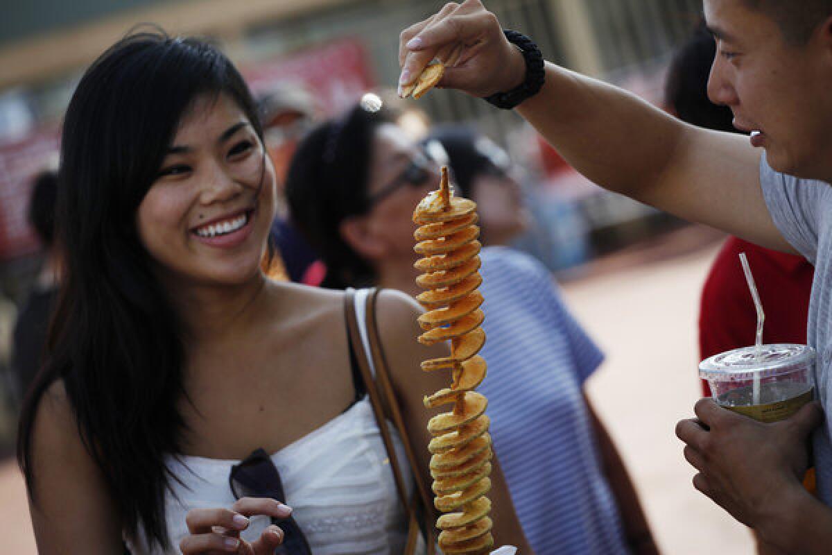 Tiffany Young and Joshua Huang enjoy a skewered fried potato from Hotato Potato, one of the most popular food booths at the 626 Night Market at Santa Anita.