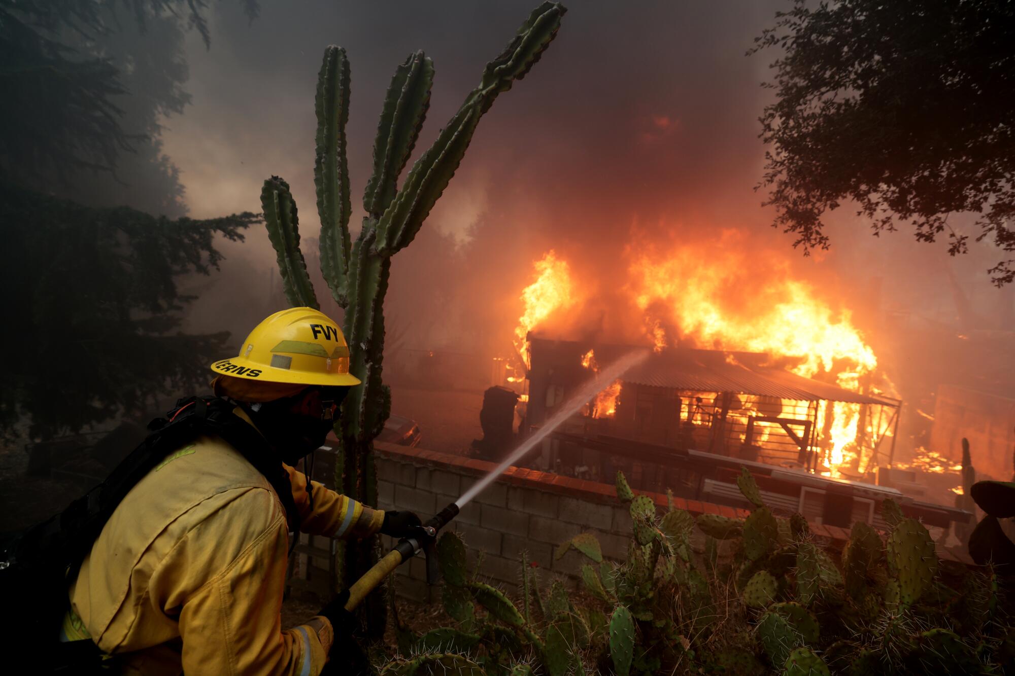 A firefighter sprays a burning house.