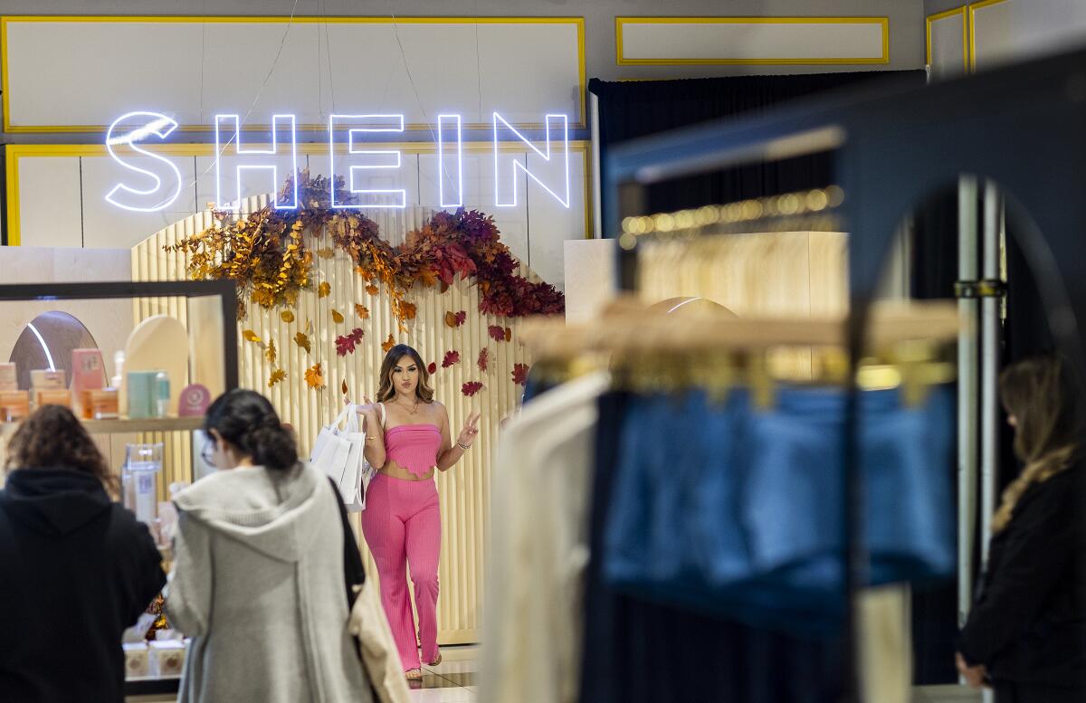 A woman in a matching pink top and pants poses in a store under a shein sign