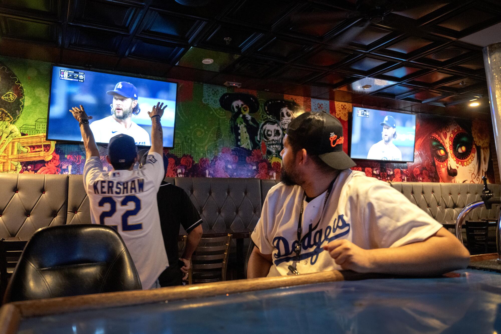 Two people in Dodgers shirts watch the game at a bar.