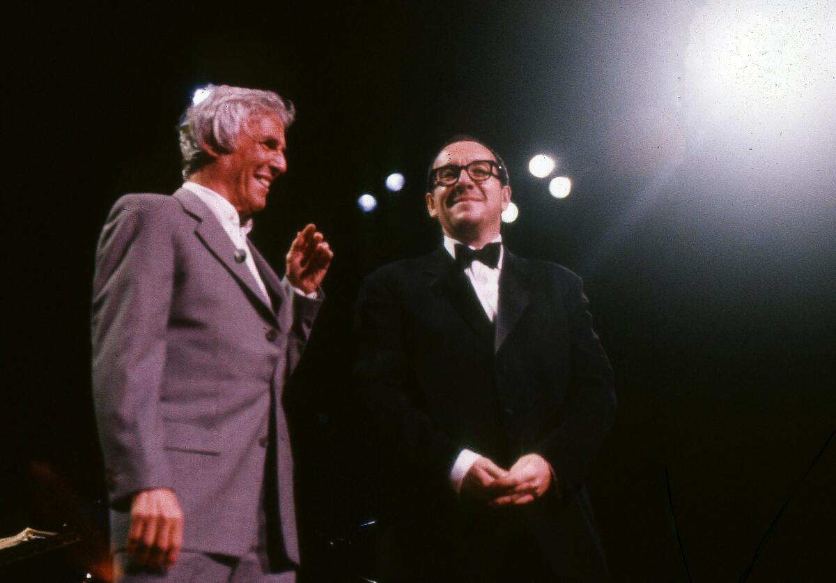 A man in a suit and a man in a tuxedo perform together onstage