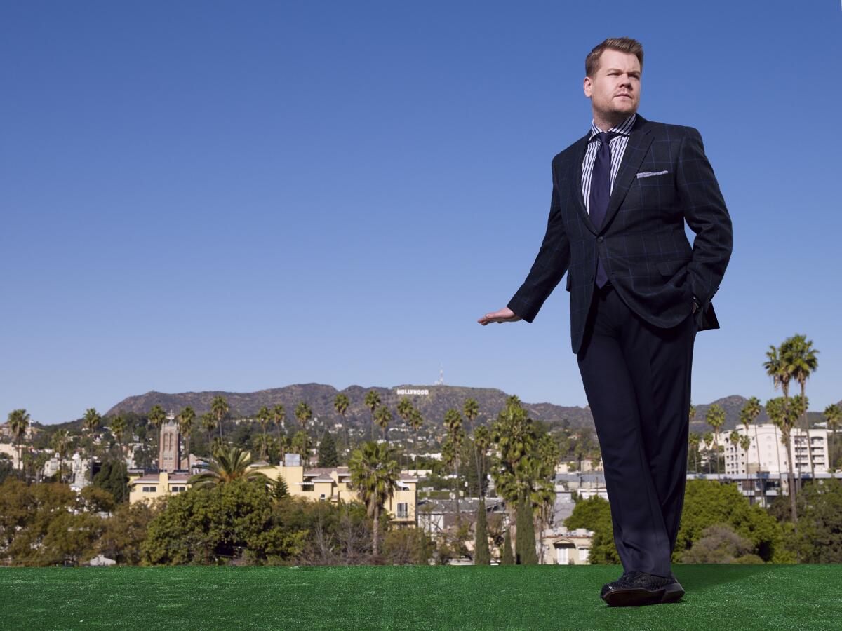 A man in a blue suit poses with mountains and blue skies in the background.